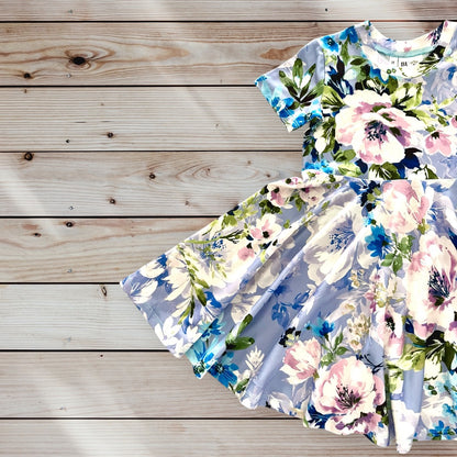 A light blue short-sleeved dress for little girls with a floral print featuring pink, white, blue, and green flowers. The dress has a full twirling skirt and a round neckline. size for ages 12 months to 12 years old. 